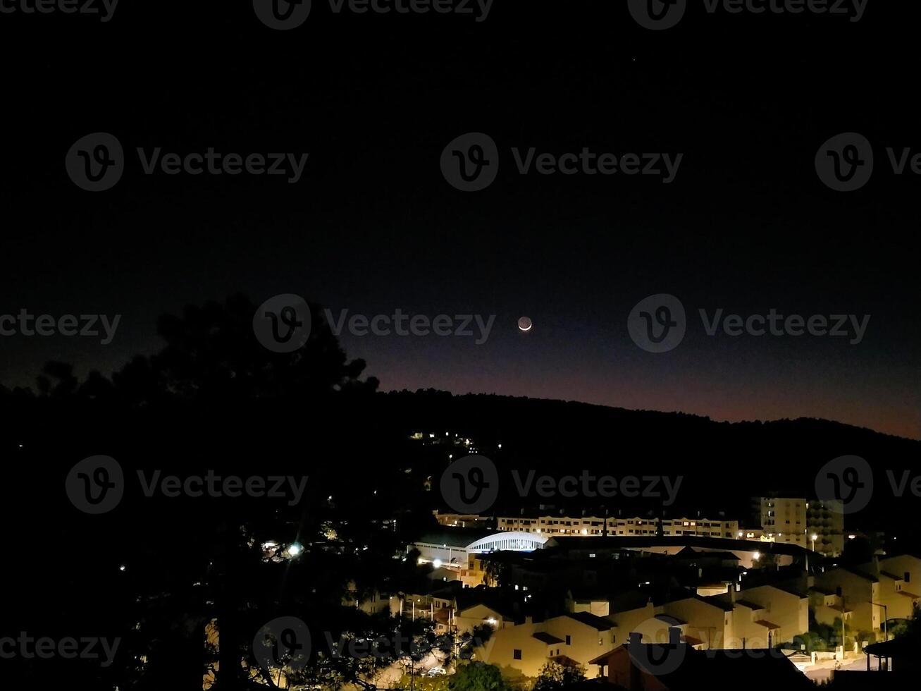 Scenic nightscape featuring a crescent moon over a dark cityscape, hinting at tranquility, mystery, and the beauty of urban life under the night sky. photo