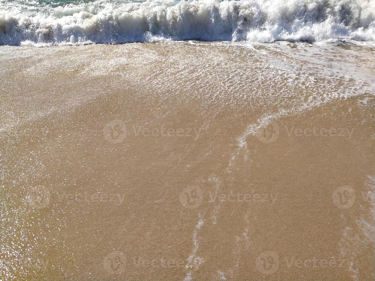 Gentle waves rolling beach at sunrise, creating bubbles and a shimmering surface photo