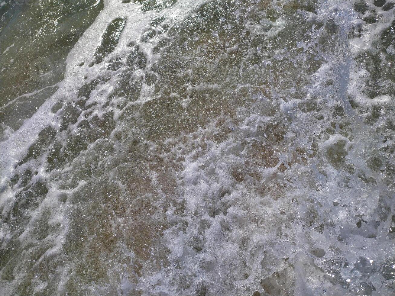 Gentle waves rolling onto sandy beach at sunrise, creating bubbles and a shimmering photo