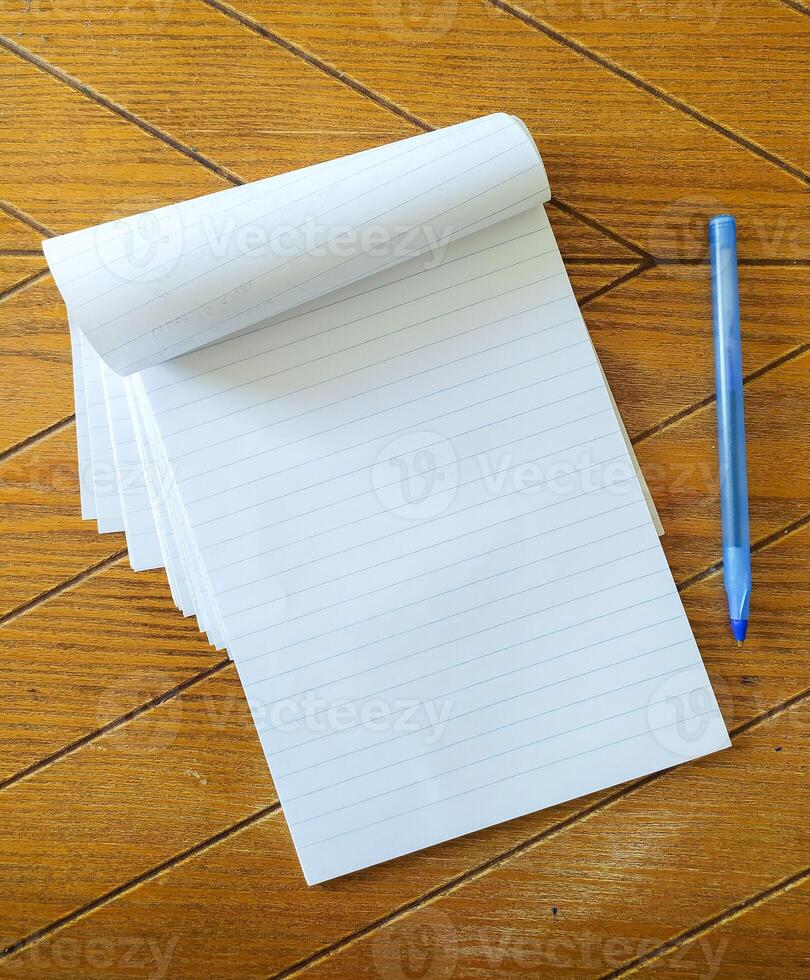 Blank lined notepad and blue pen on a wood desk. Perfect for concepts of writing, planning, education, or office supplies. Great for blogs, websites, or social media. photo