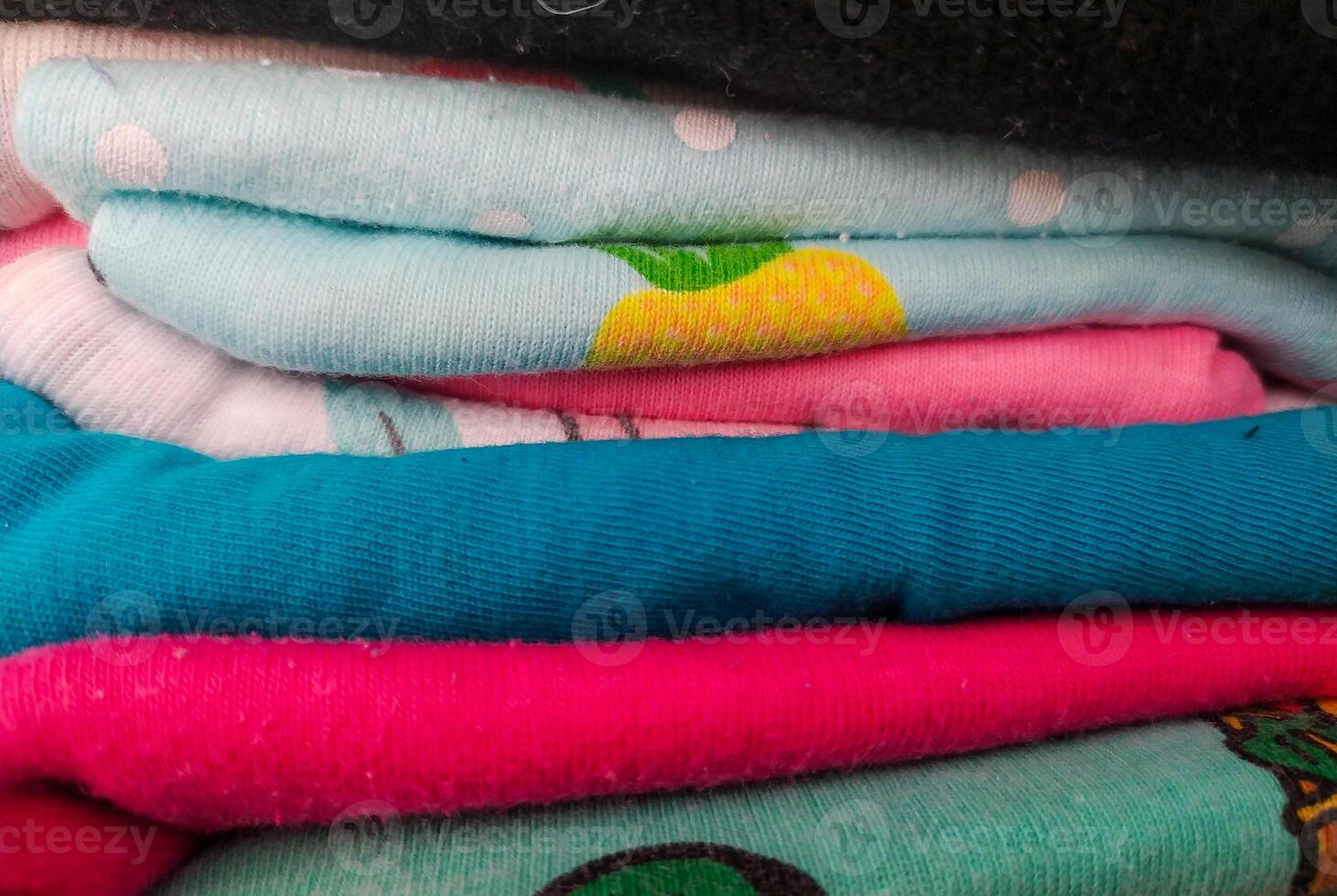 Neatly folded colorful apparel. A closeup showcasing a pile of vibrant shirts. Perfect for themes like organization, textiles, fashion, comfort, or domestic routines. photo