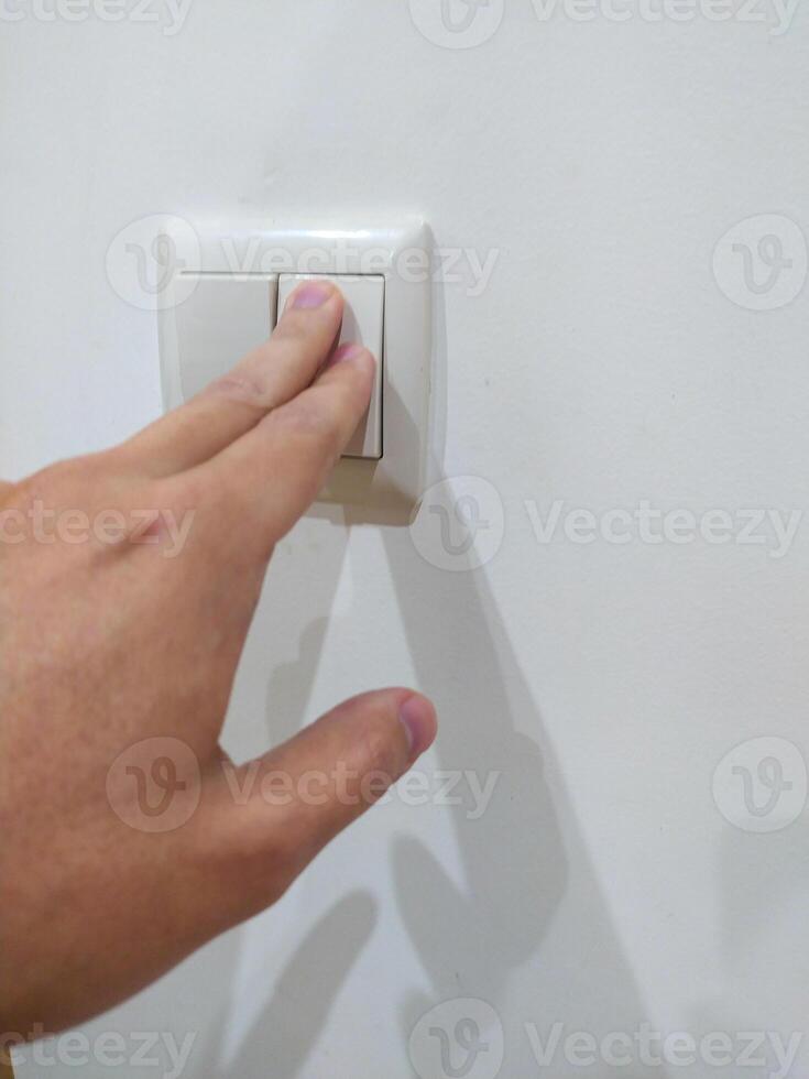 Hand pressing light switch on white wall. Symbolizes control, power, action, and efficiency. Good for energy, technology, and lifestyle themes. Clean and simple. photo