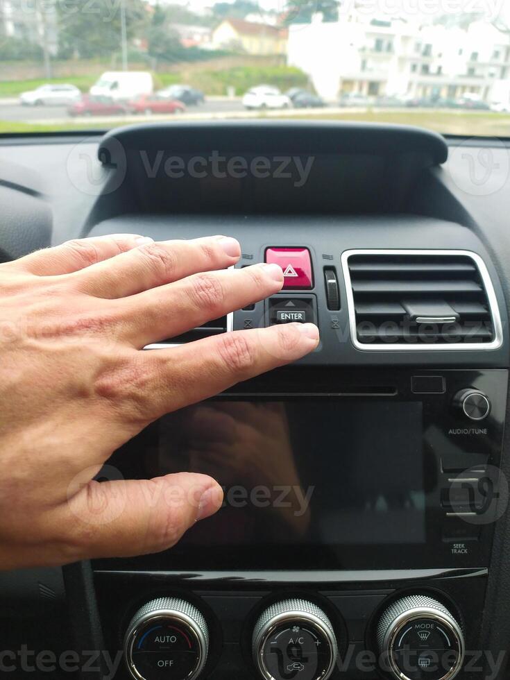 Closeup of a hand reaching for a cars hazard lights button. Illustrates roadside assistance, emergency situations, or car safety. Perfect for automotive, insurance, or travel websites. photo