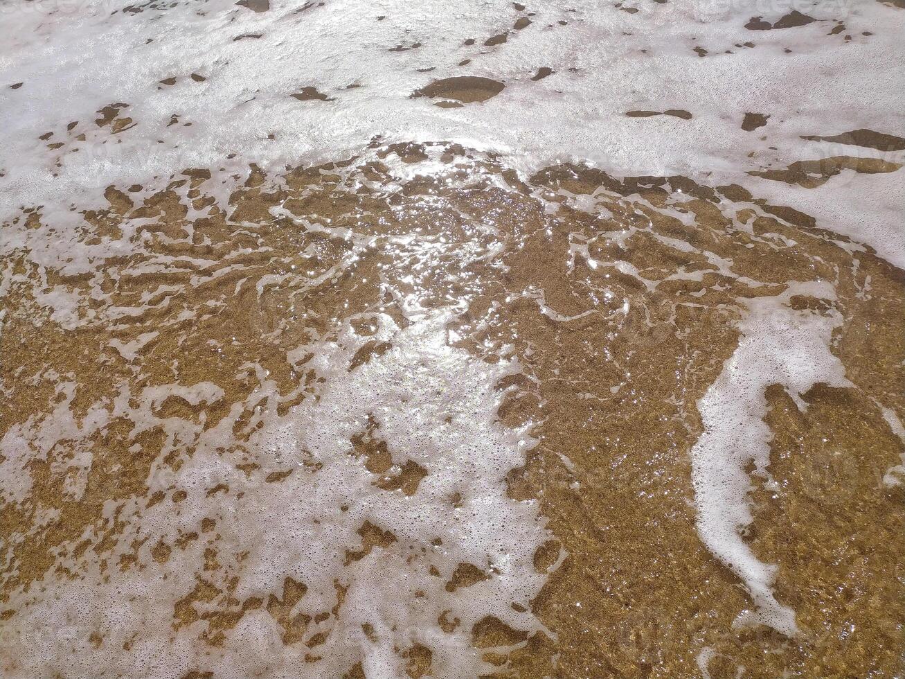 Gentle waves rolling onto sandy beach at sunrise, creating bubbles and a photo
