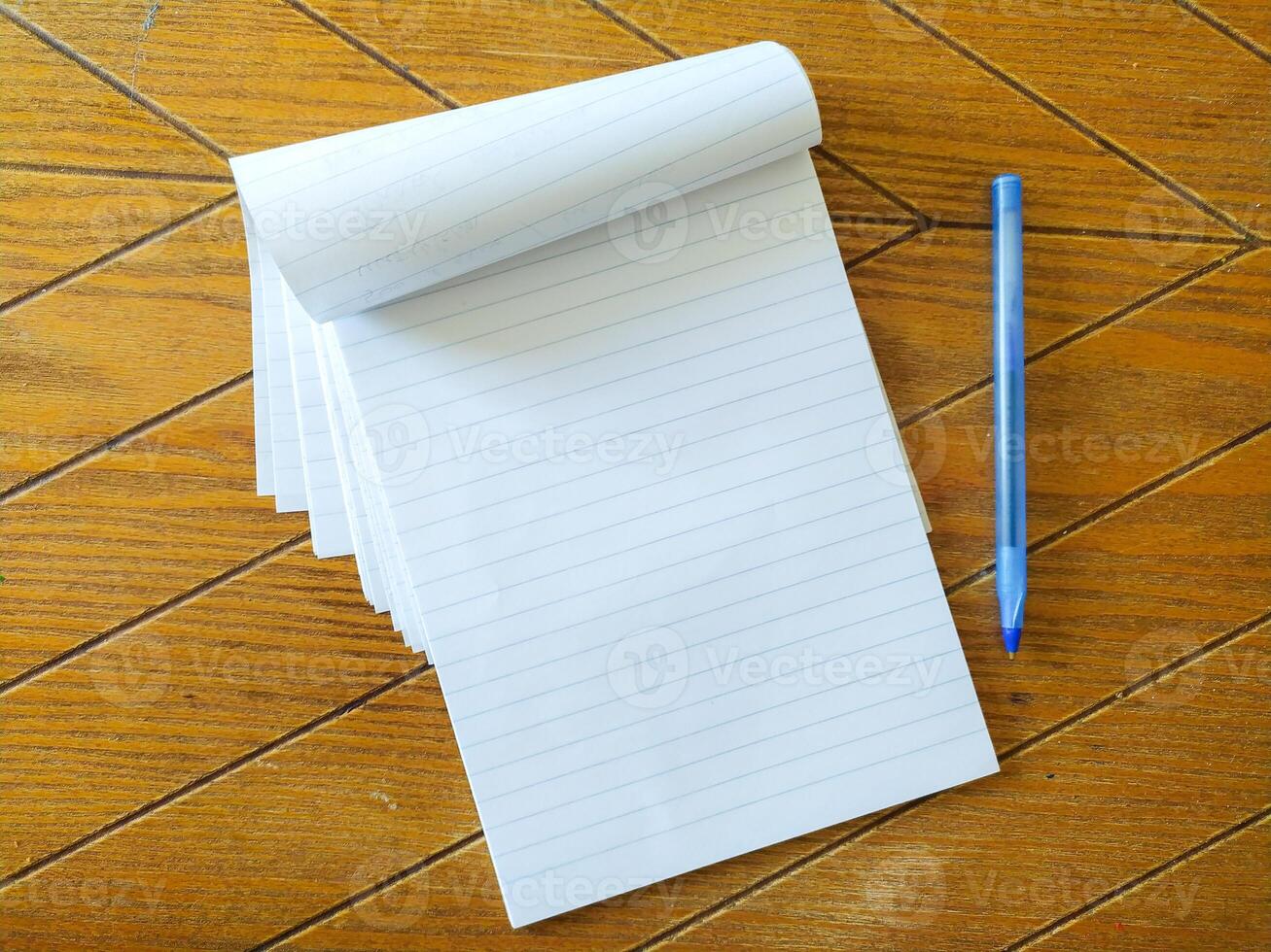 Blank lined notepad and blue pen on a wood table. Perfect for education, business, or office concepts. Clean, simple, and ready for your message. Ideal for mockups or website backgrounds. photo