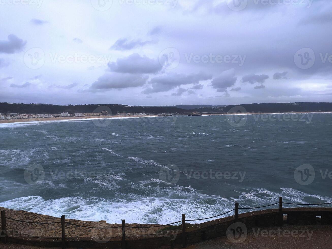 Dramatic seascape featuring turbulent ocean waves crashing against a distant shore under a cloudy sky. Evokes feelings of power, natures force, and coastal beauty. photo