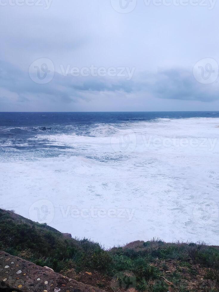 Dramatic ocean view with powerful waves crashing against the shore under a moody sky. Evokes feelings of strength, resilience, natural beauty. Perfect for travel, weather, emotional concepts. photo