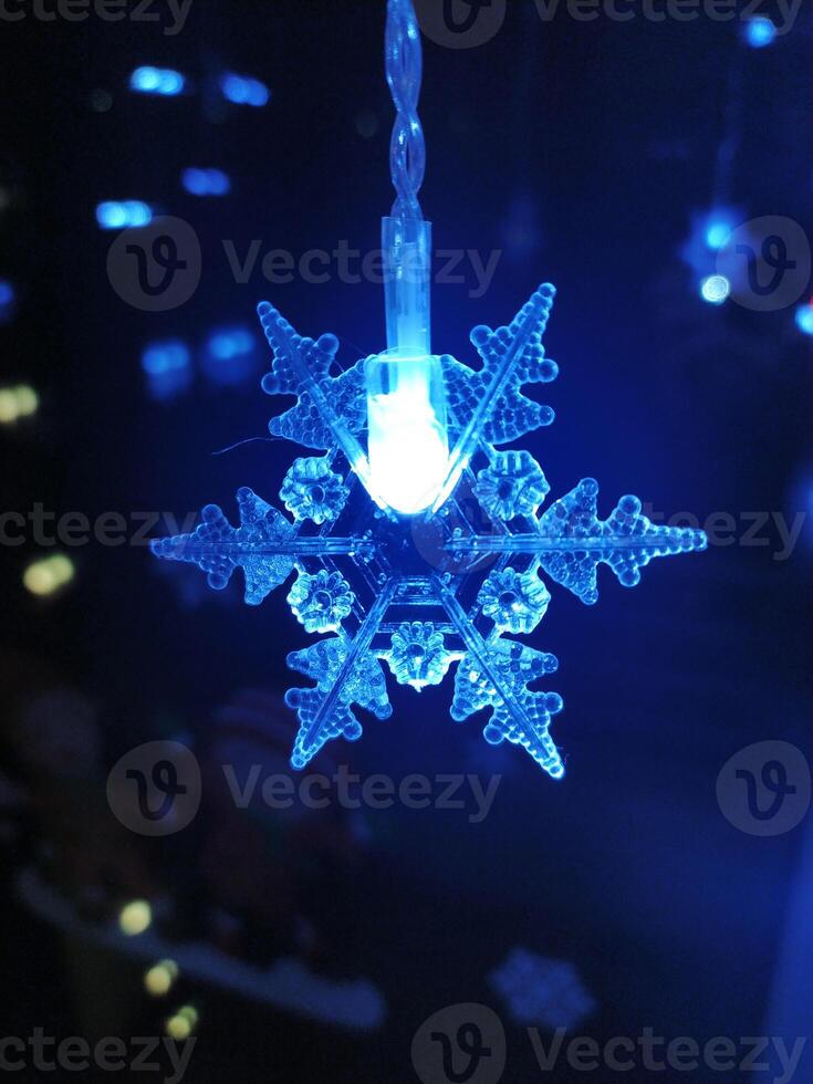 Glowing blue snowflake LED light hanging against a dark background. Perfect for winter, holiday, or festive designs. Creates a magical, atmospheric mood. photo