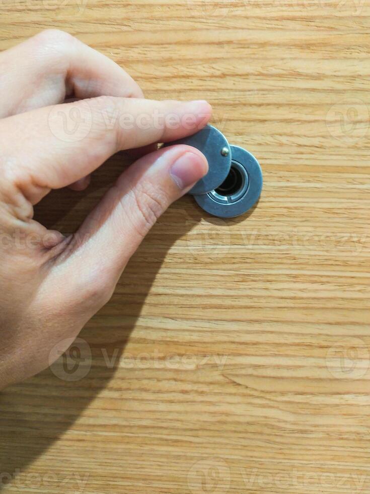 Hand opening peephole cover on a wood door, closeup. Represents privacy, security, and anticipation. Use for home safety, access control, and property themes. photo