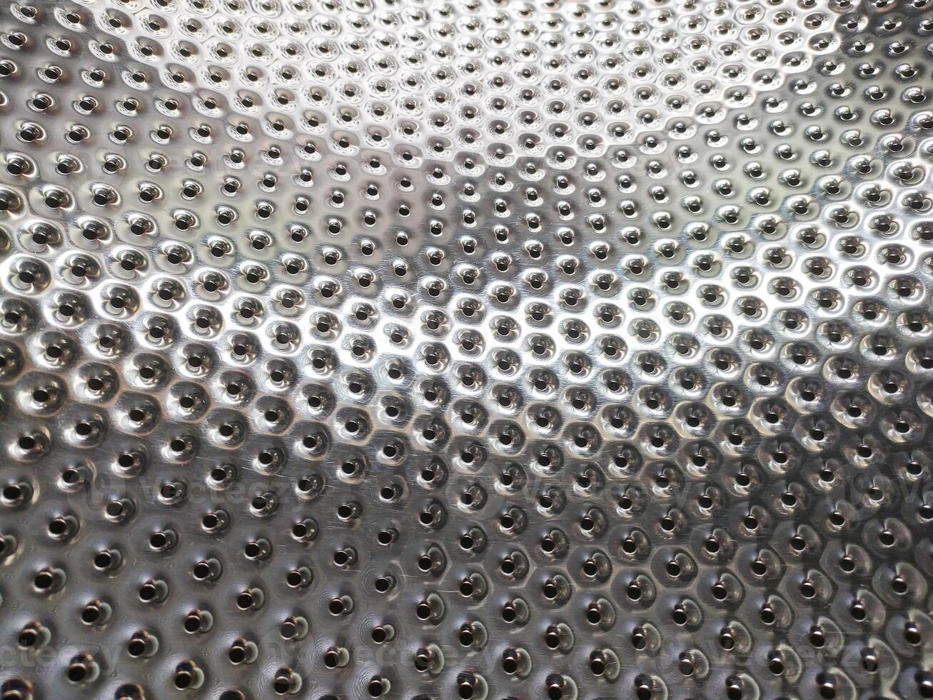 Shiny, dimpled metallic surface with repeating holes. Abstract pattern perfect for backgrounds, textures, or representing industrial concepts like engineering or manufacturing. photo