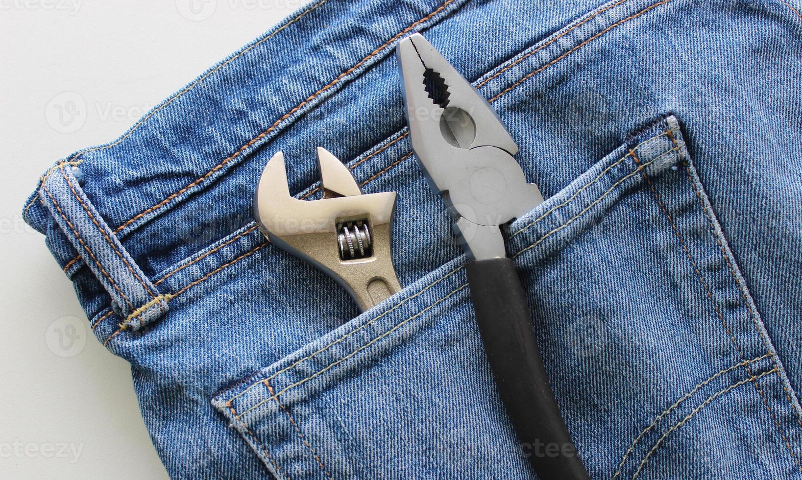 Adjustable wrench and pliers with one untucked handle in a jeans pocket. Detailed stock photo for home tools illustration