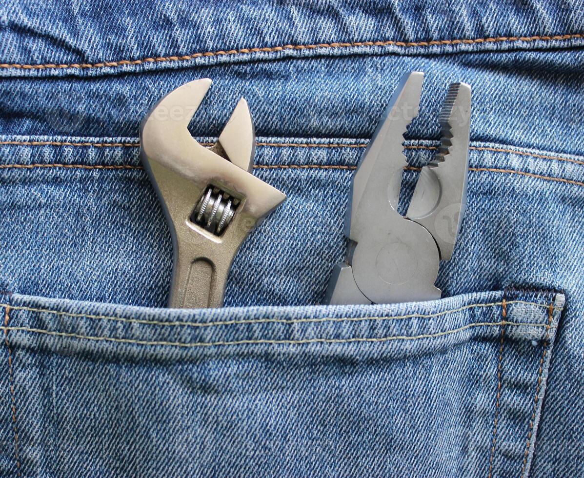 An adjustable spanner and pliers are placed in a jeans pocket. Closeup stock image for home repair theme photo