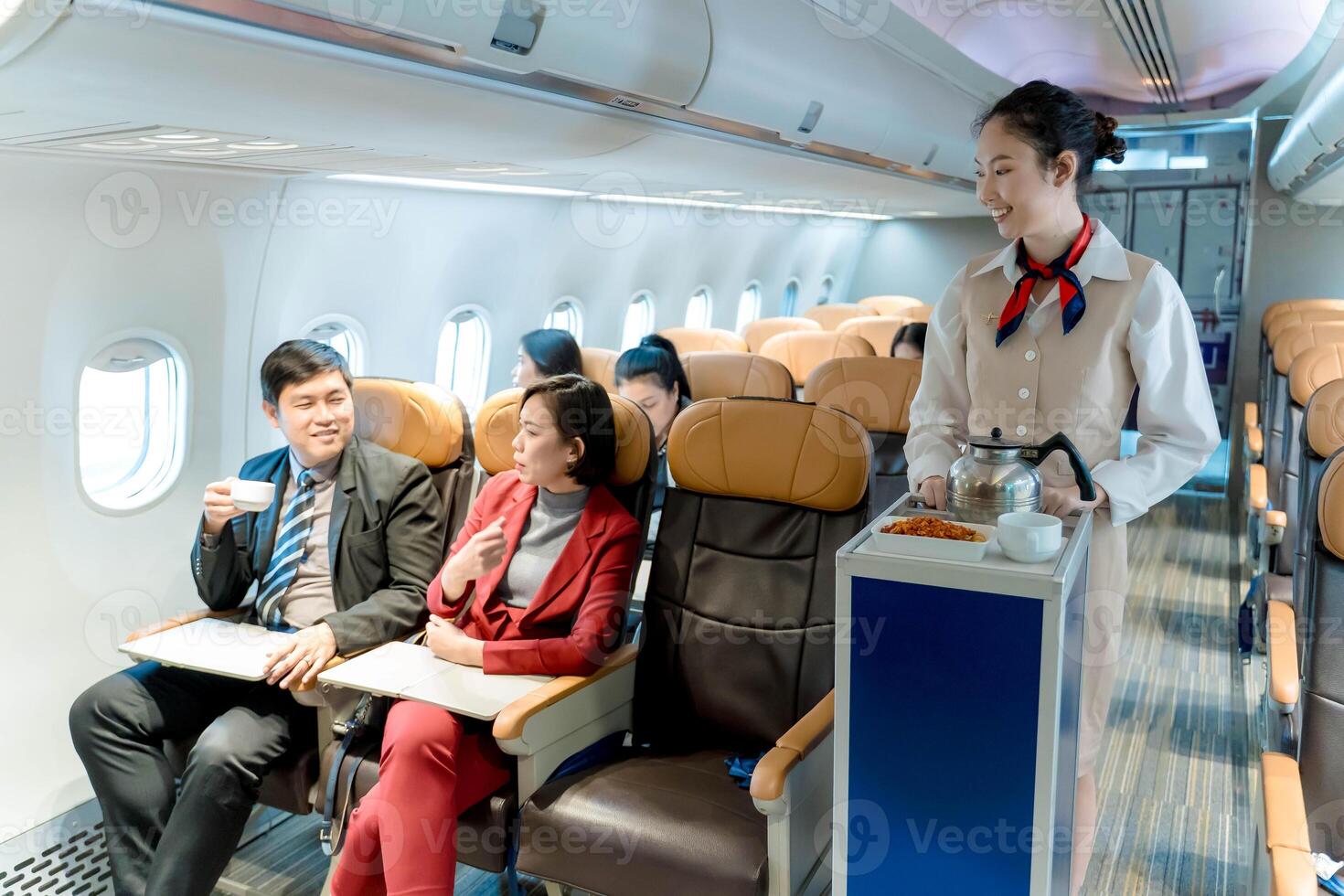 Flight attendant serving inflight meal and beverage with trolley to smiling business passengers on airplane during flight, showcasing professional airline service photo