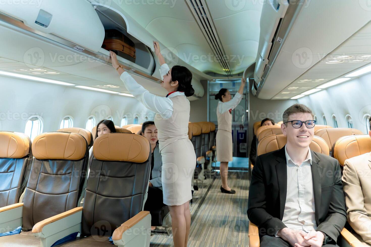 Flight attendants assist passengers by closing overhead luggage bins inside airplane cabin, ensuring safety and readiness before departure on a commercial flight photo
