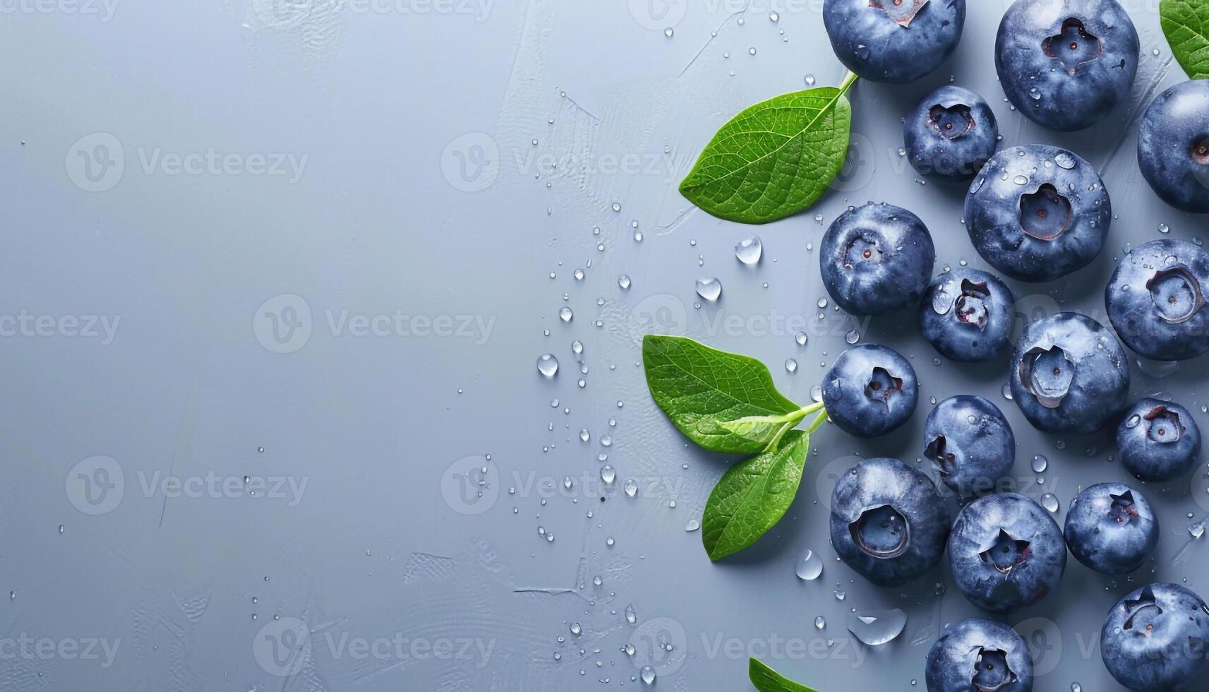 Fresh blueberries with green leaves and water droplets on blue background with copy space top view photo