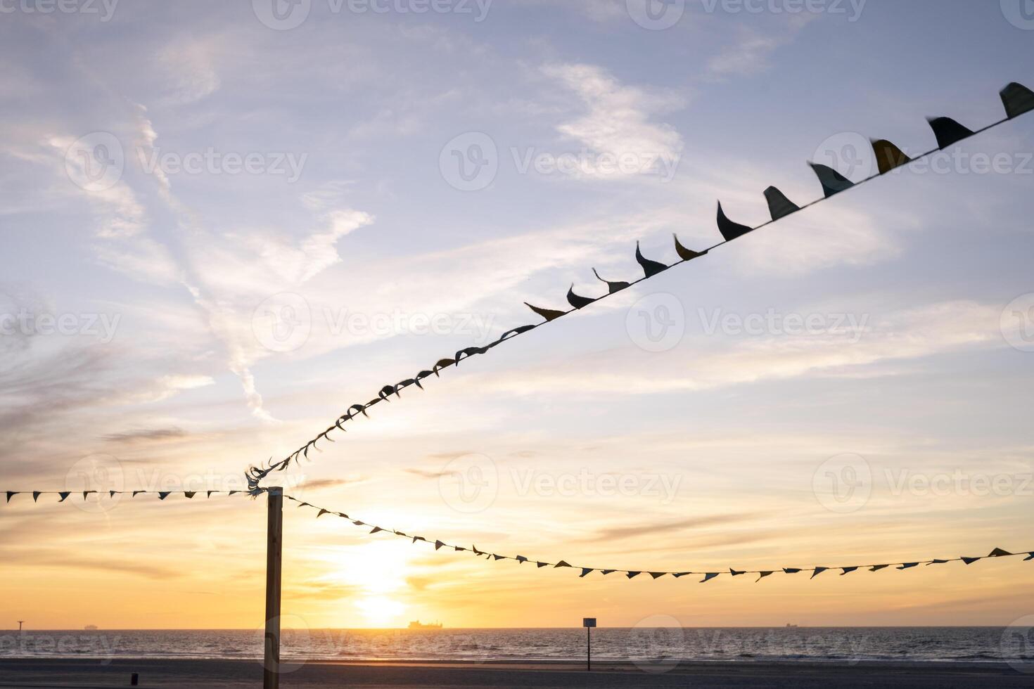 Colorful flags silhouetted against a serene beach sunset with soft clouds, creating a peaceful and abstract coastal atmosphere. photo