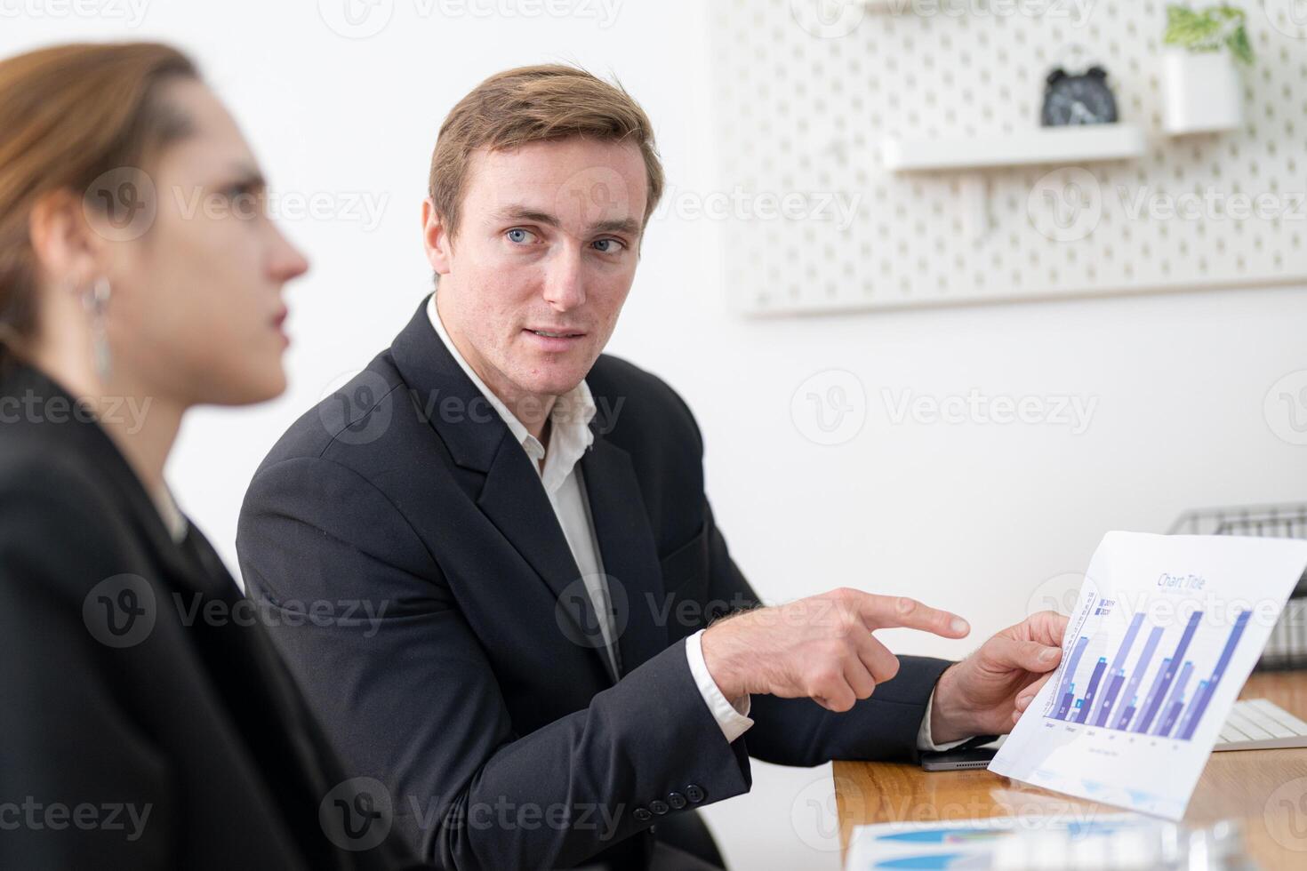 Business professional presents data analysis to a colleague during an office meeting in a modern workspace photo