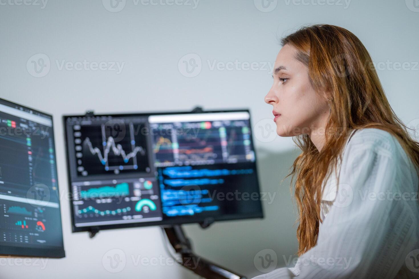 Professional woman analyzes data and financial trends on multiple computer screens in a modern office setting photo