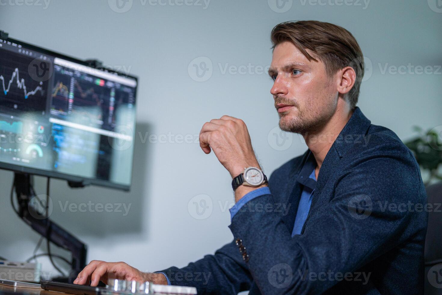 Professional man analyzing financial data in a modern office setting with multiple screens during daytime hours photo