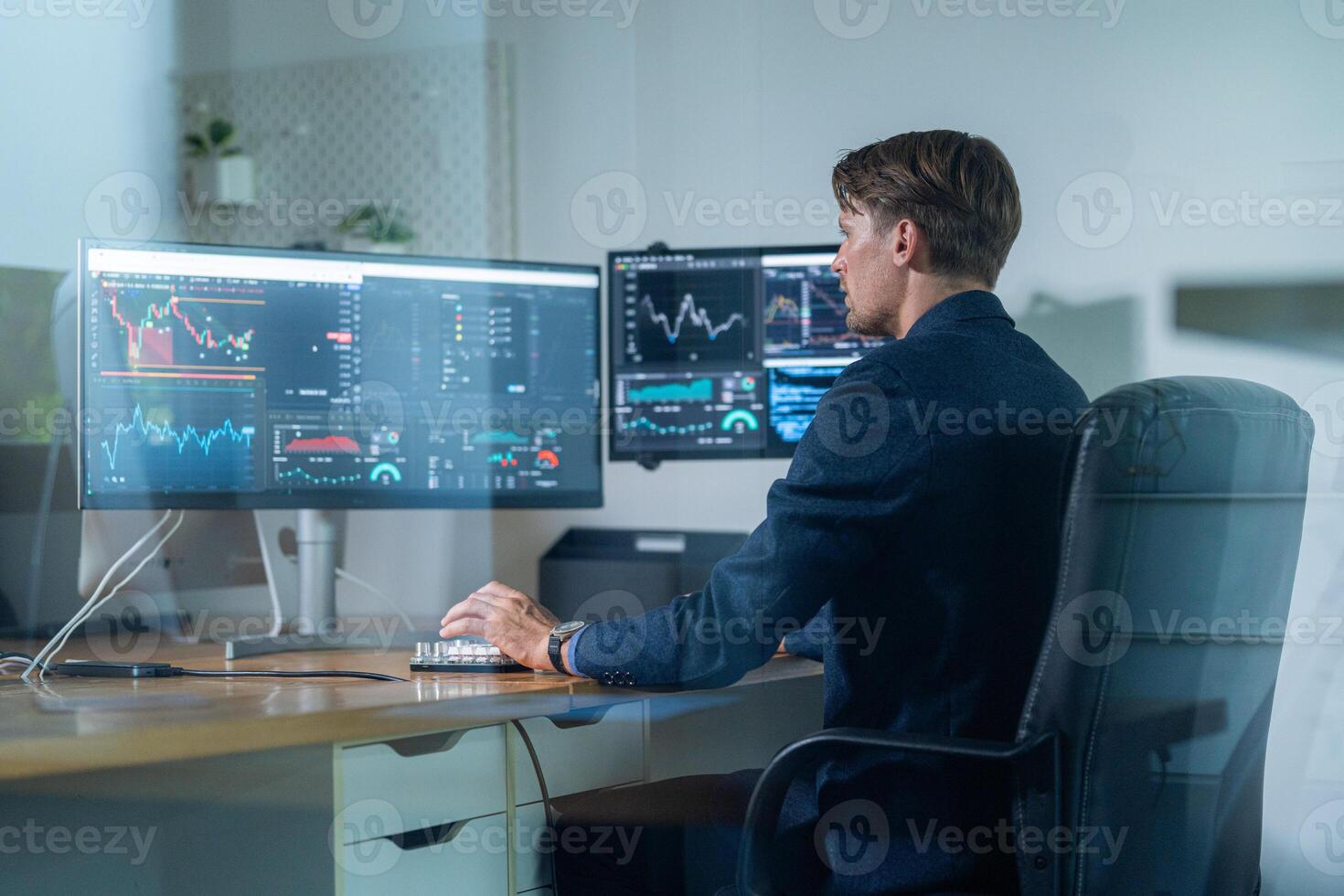 Professional working at multiple computer screens while analyzing stock market data in a modern office environment photo