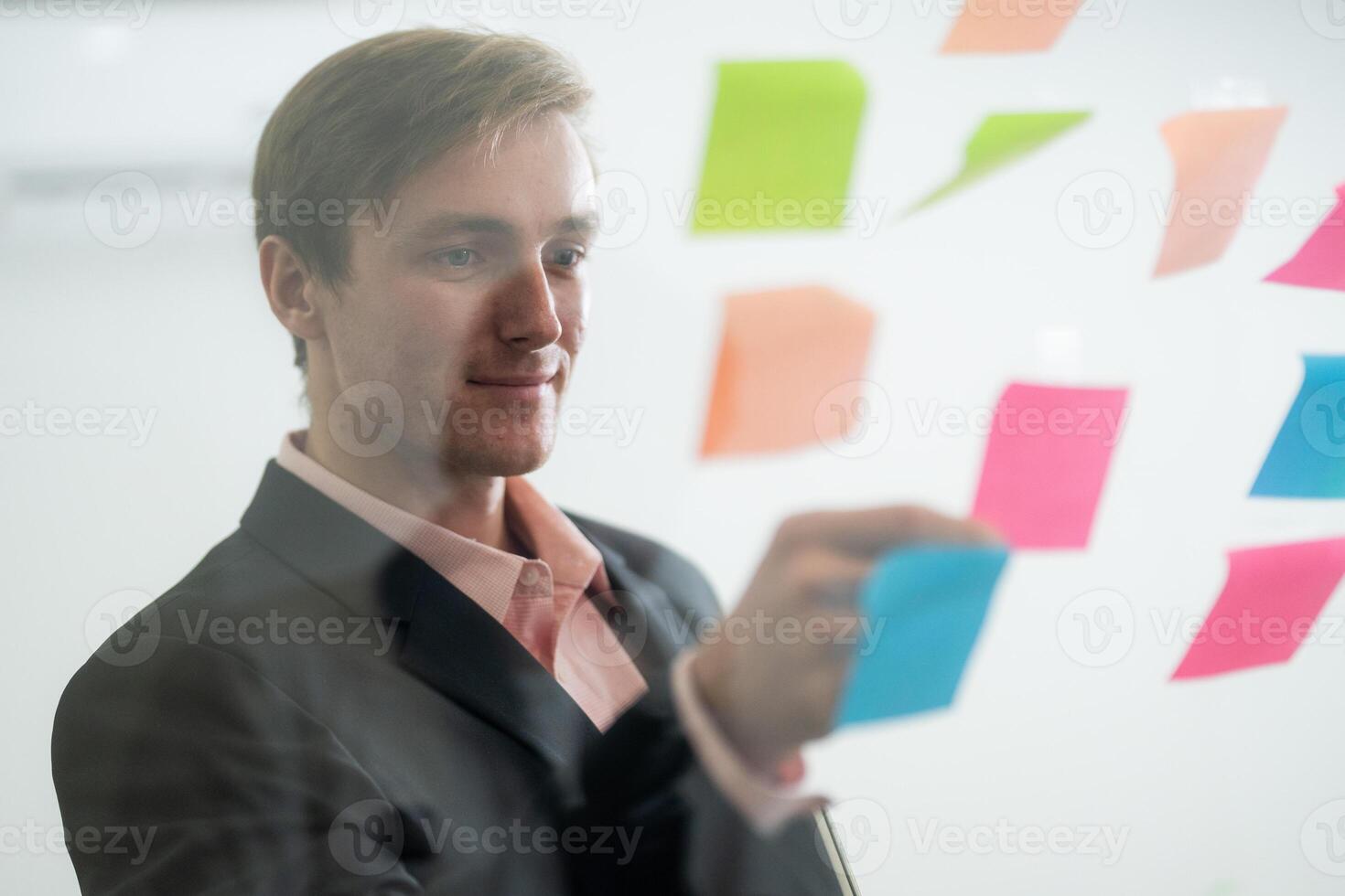 Professional man organizing colorful sticky notes on a glass wall during a brainstorming session at a modern office photo