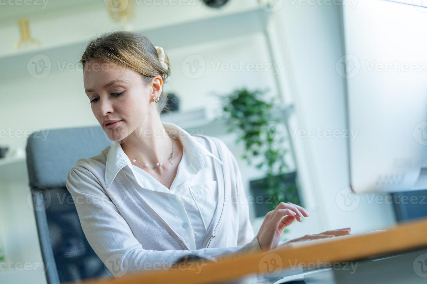 Woman working at a desk in a modern office setting during daylight hours focused on her tasks and engaged in her work photo