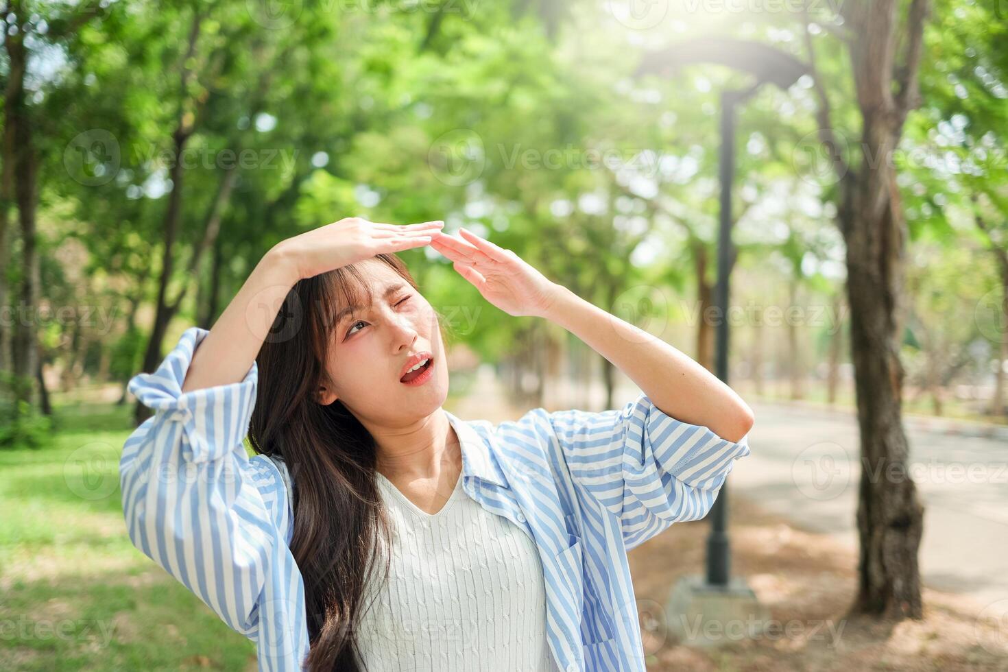 Young Asian woman walking in the park having sunstroke in summer hot weather, Young pretty girl drying sweat using a wipe on a warm summer day in a park photo