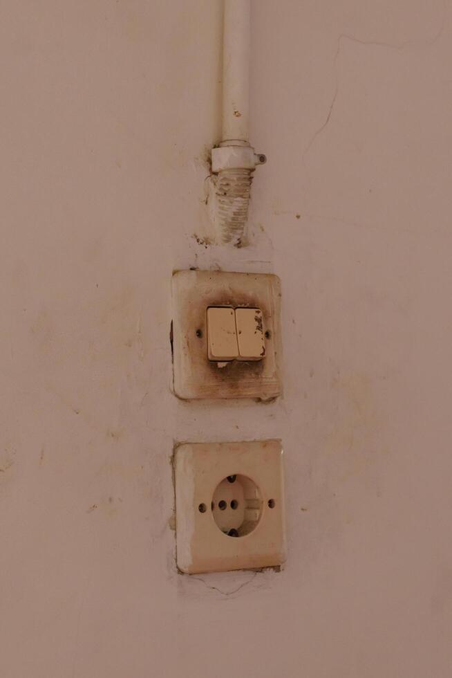 Old electrical switch and socket on wall showing signs of dirt and damage photo