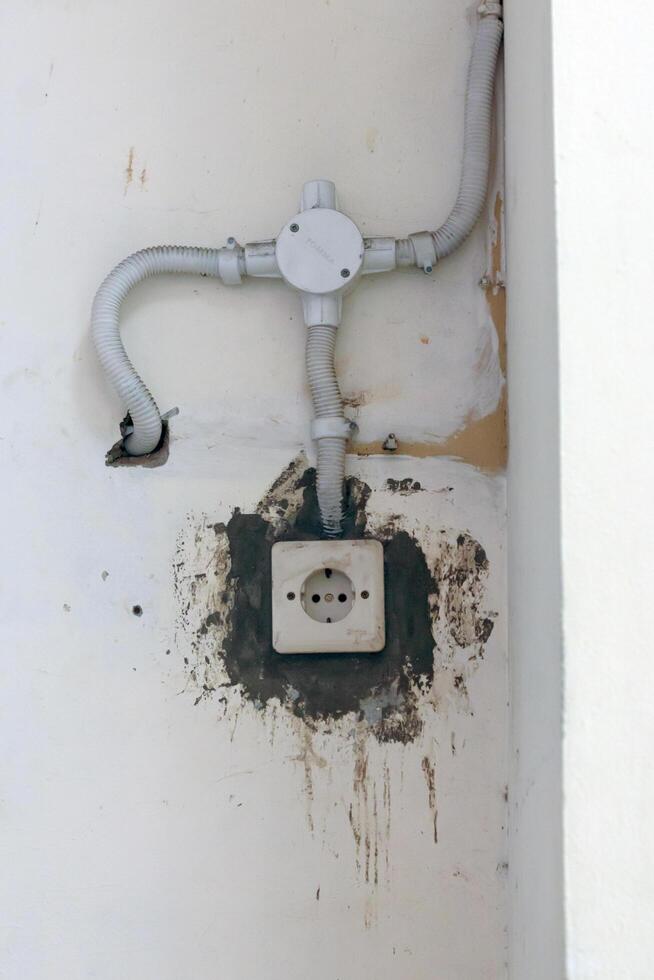 Old wall power outlet with visible dirt and exposed wiring, perfect for illustrating neglected electrical infrastructure, decay, or maintenance issues photo