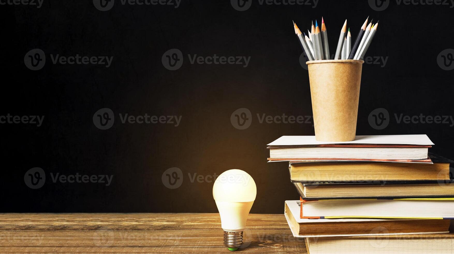 Light bulb is lit up on a table with a stack of books and pencils photo