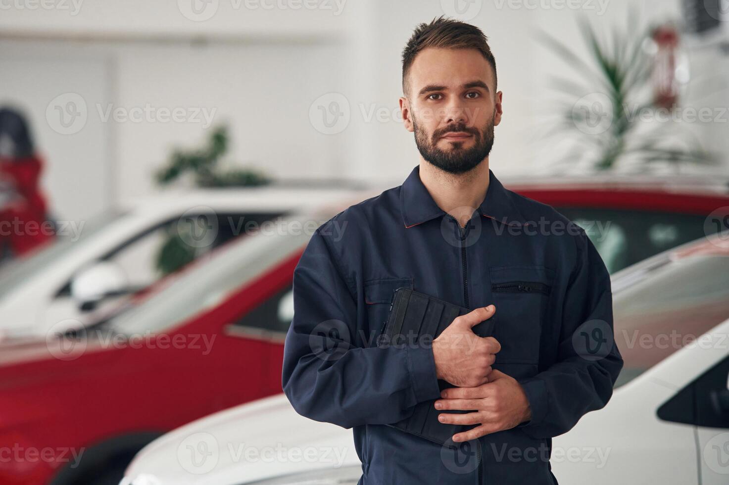 In blue ,,colored ,uniform. Car repairman is in the garage with automobile photo