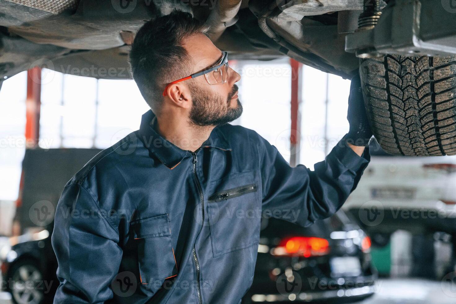 Under the vehicle, fixing,. Car repairman is in the garage with automobile photo