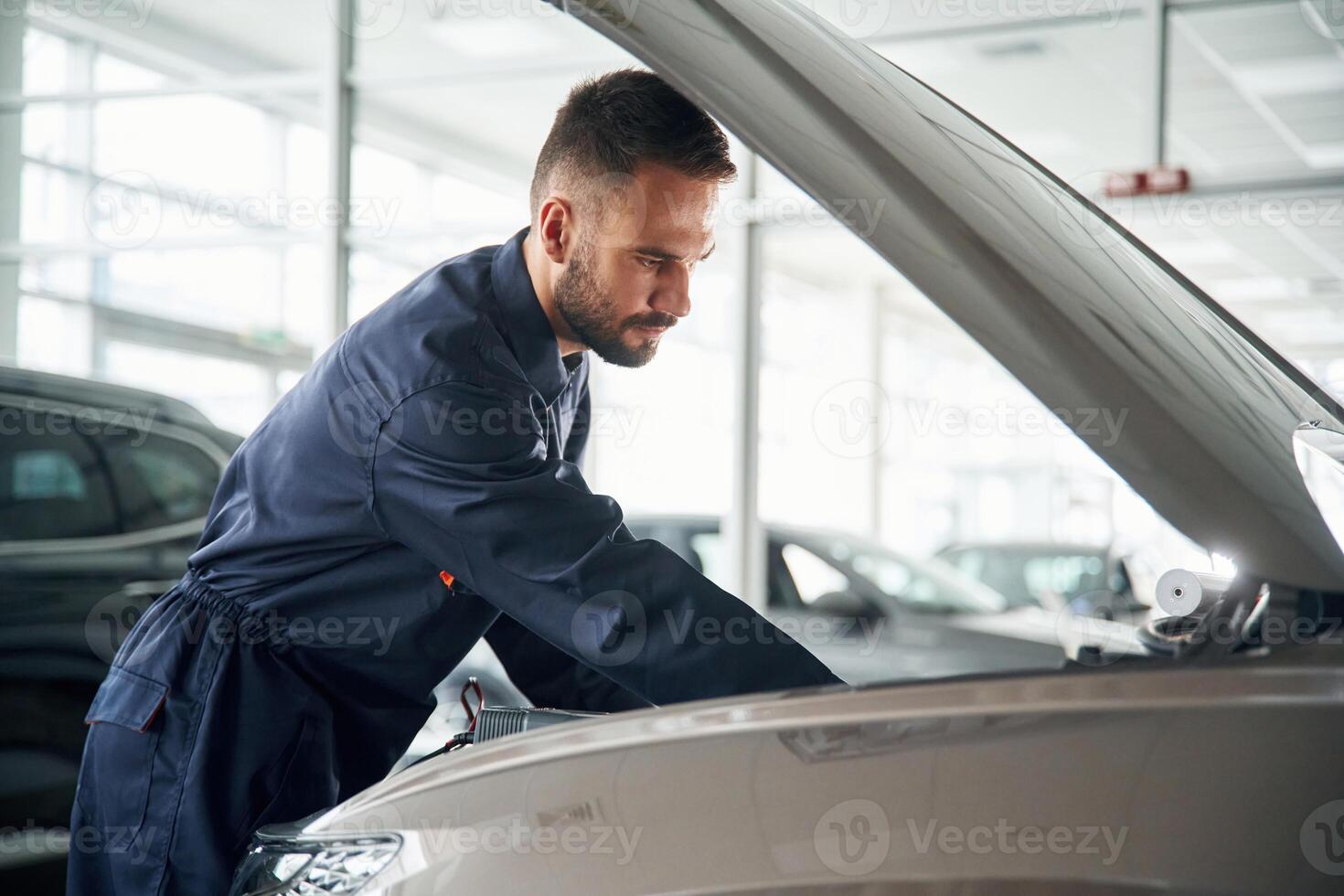 Hood of vehicle is,, opened. Car repairman is in the garage with automobile photo