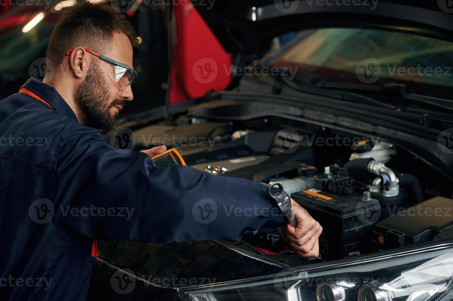 In ,blue ,colored uniform. Car repairman is in the garage with automobile photo