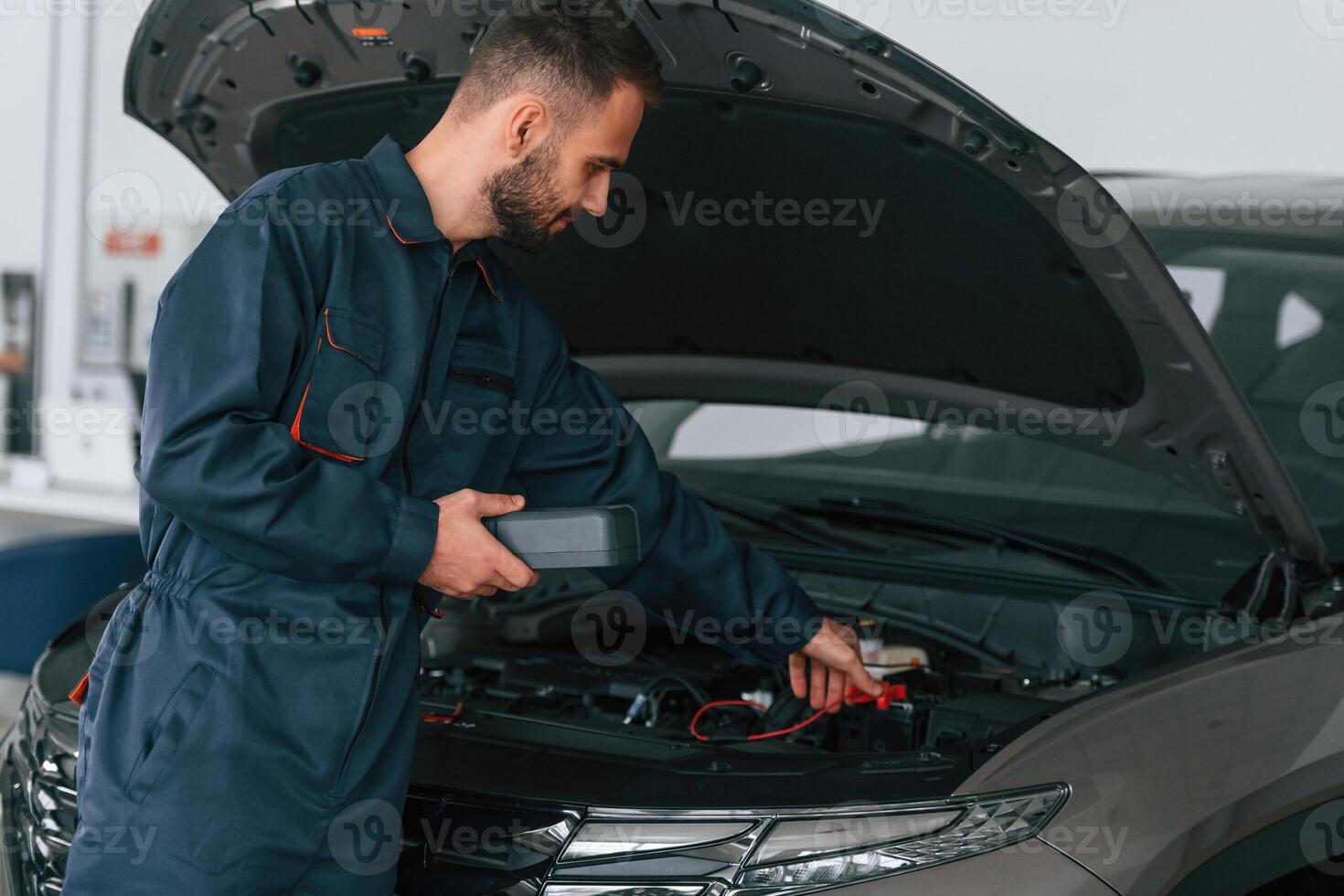 With device for measuring, electricity.. Car repairman is in the garage with automobile photo