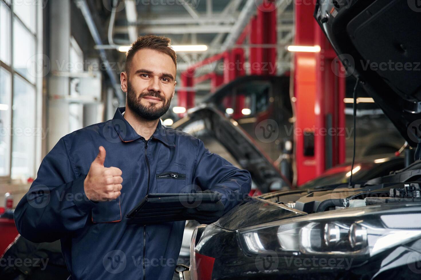 Using ,tablet.. Car repairman is in the garage with automobile photo