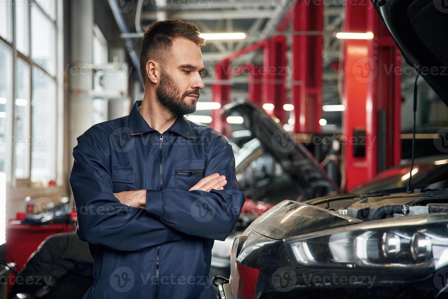 With, arms ,crossed, standing. Car repairman is in the garage with automobile photo