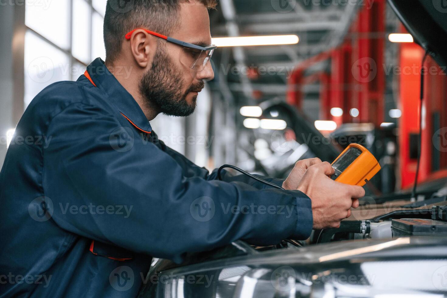 Yellow colored device for measuring ,electricity is in hands. Car repairman is in the garage with automobile photo