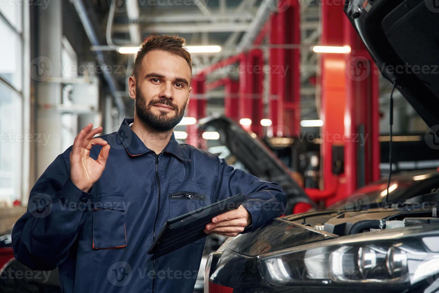 Using ,,tablet. Car repairman is in the garage with automobile photo