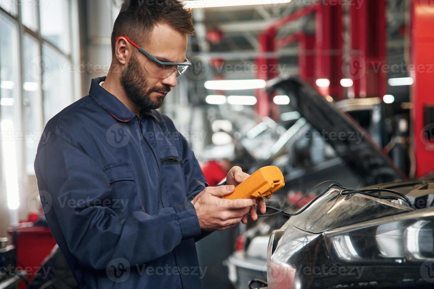 Checking electronics by ,,using device. Car repairman is in the garage with automobile photo