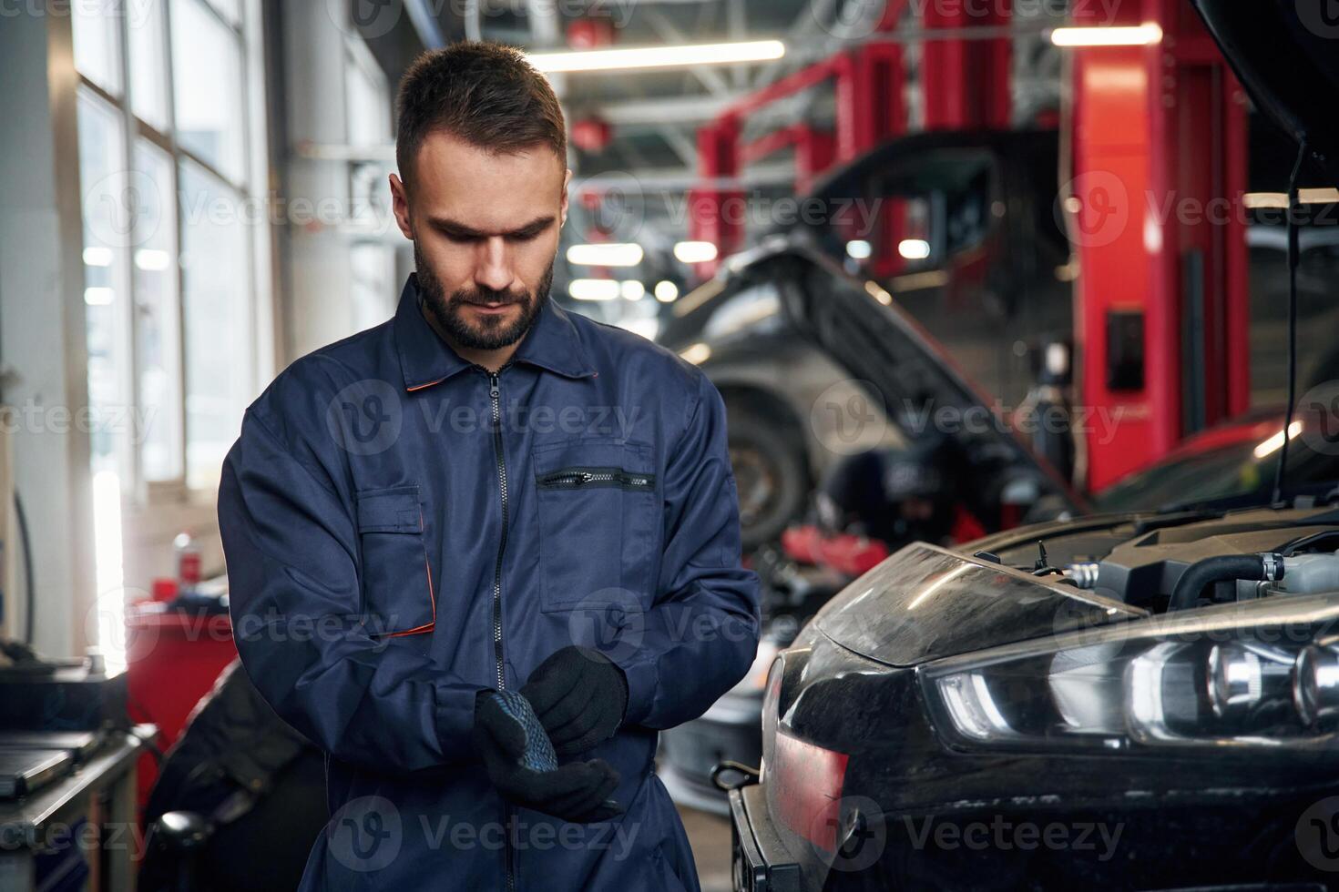 Wearing the, gloves, standing. Car repairman is in the garage with automobile photo