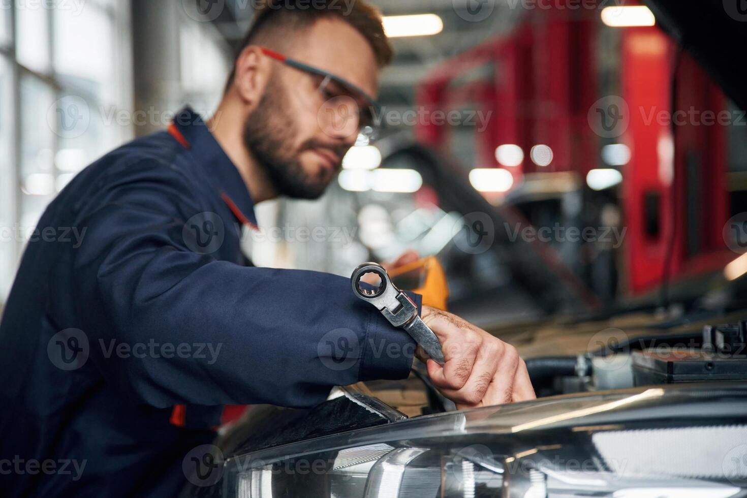 Professional electro device, in hands. Car repairman is in the garage with automobile photo