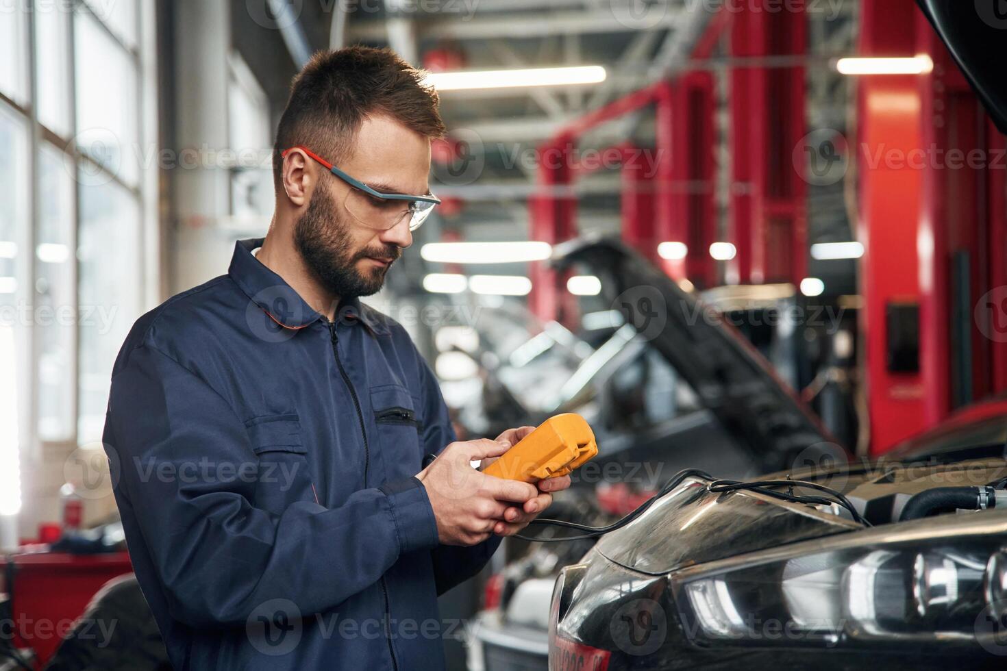 Professional ,electro device in hands. Car repairman is in the garage with automobile photo