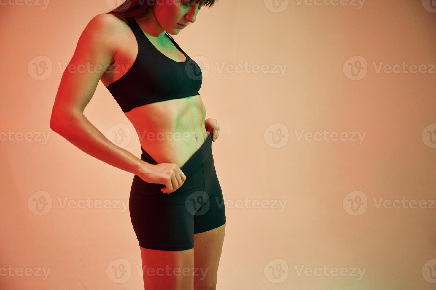 Showing, abs, standing. Young woman in fitness clothes is in the studio photo