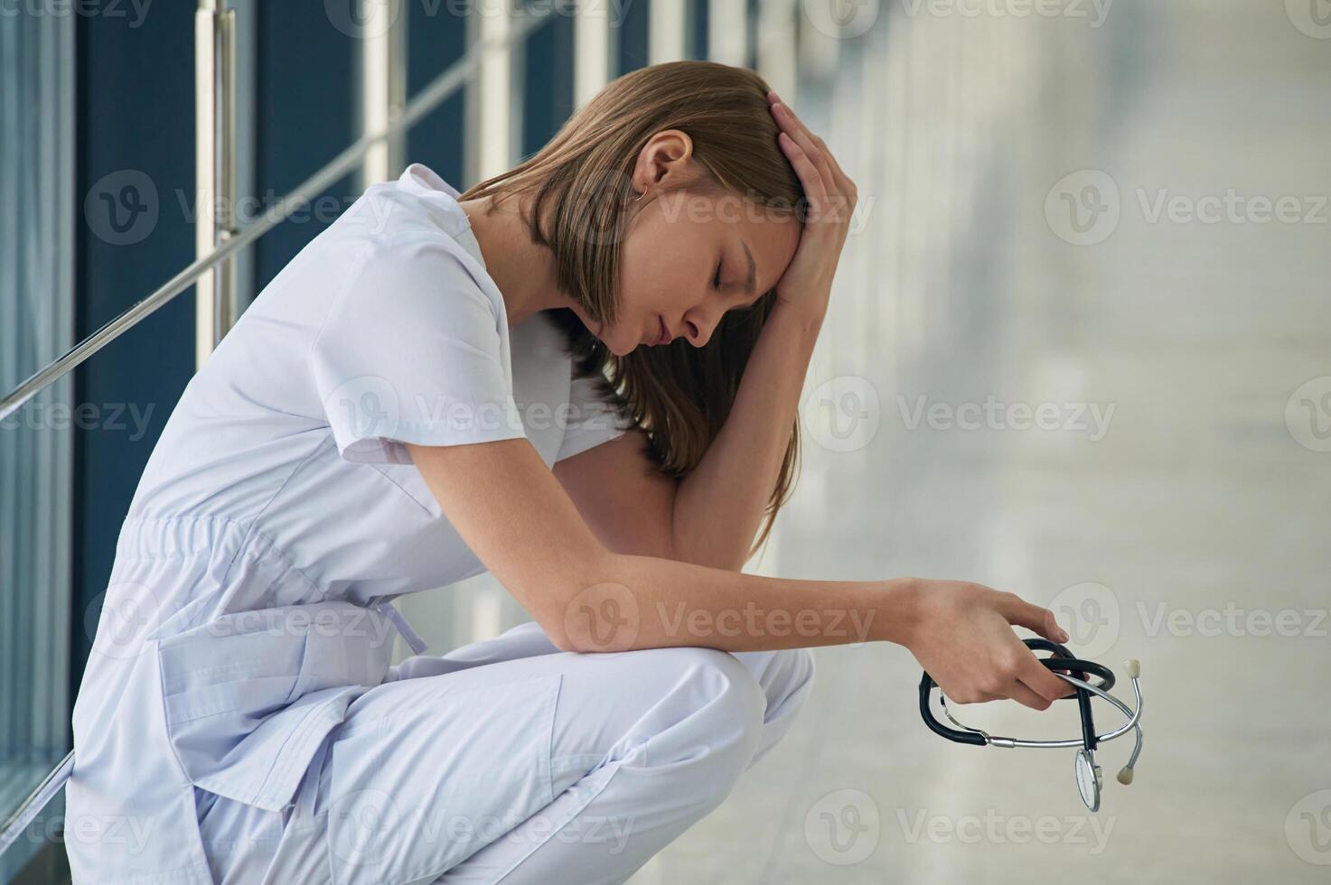 Sitting, taking a break, tired. Female doctor in white coat is in the hall photo