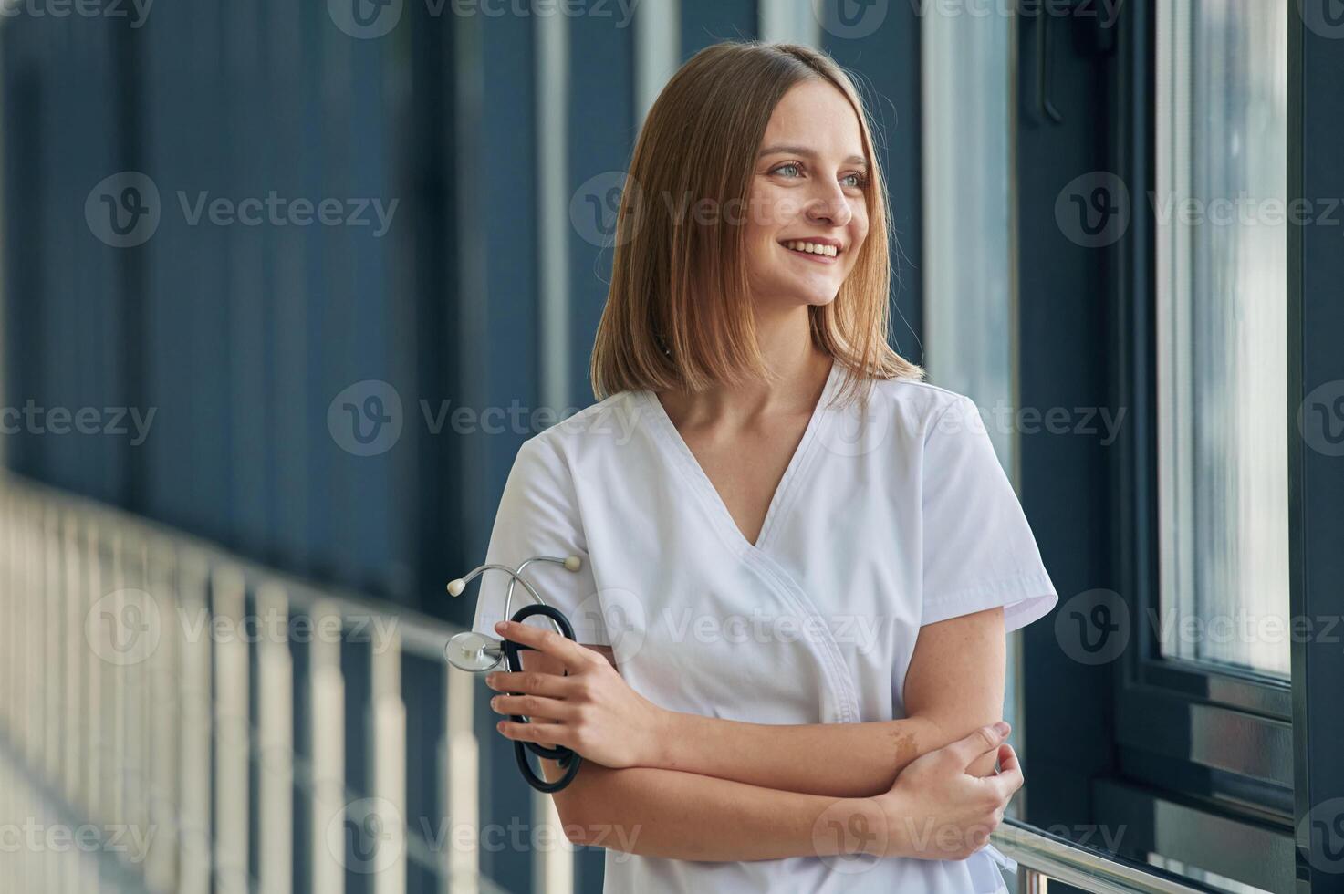 Standing, with arms crossed. Female, doctor in white coat is in the hall photo