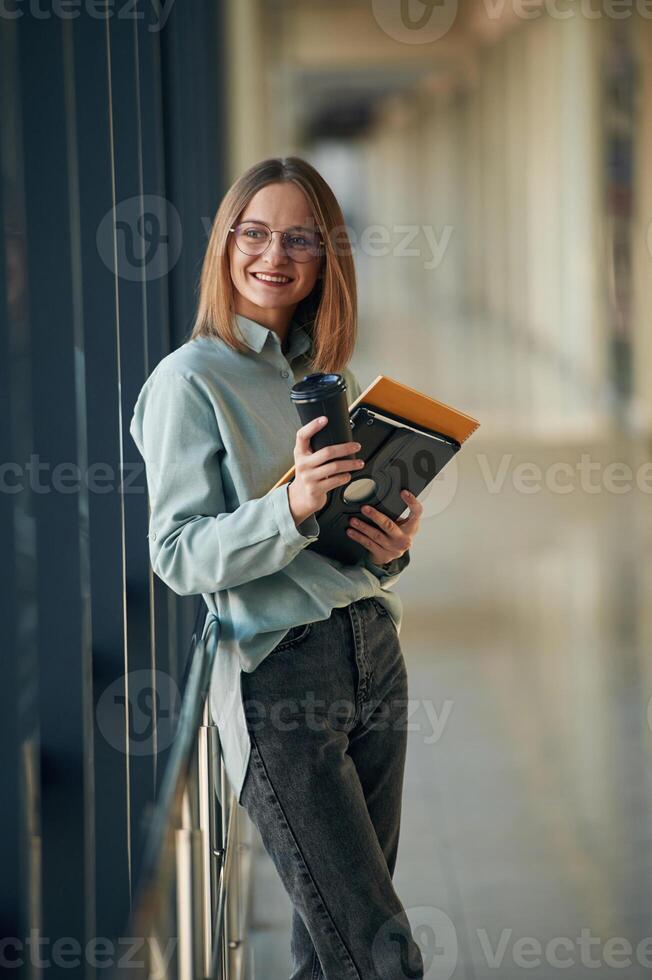 Drink, notepad ,and tablet ,,in hands. Young woman in airport hall photo