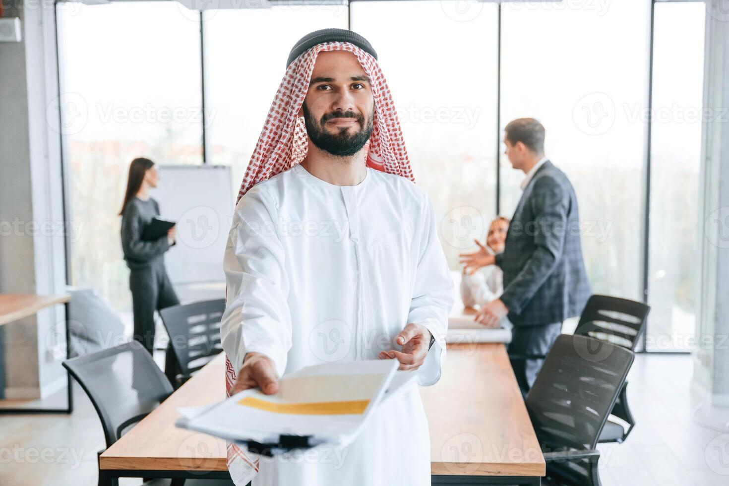 People behind Muslim businessman that is in traditional outfit with colleagues in office photo