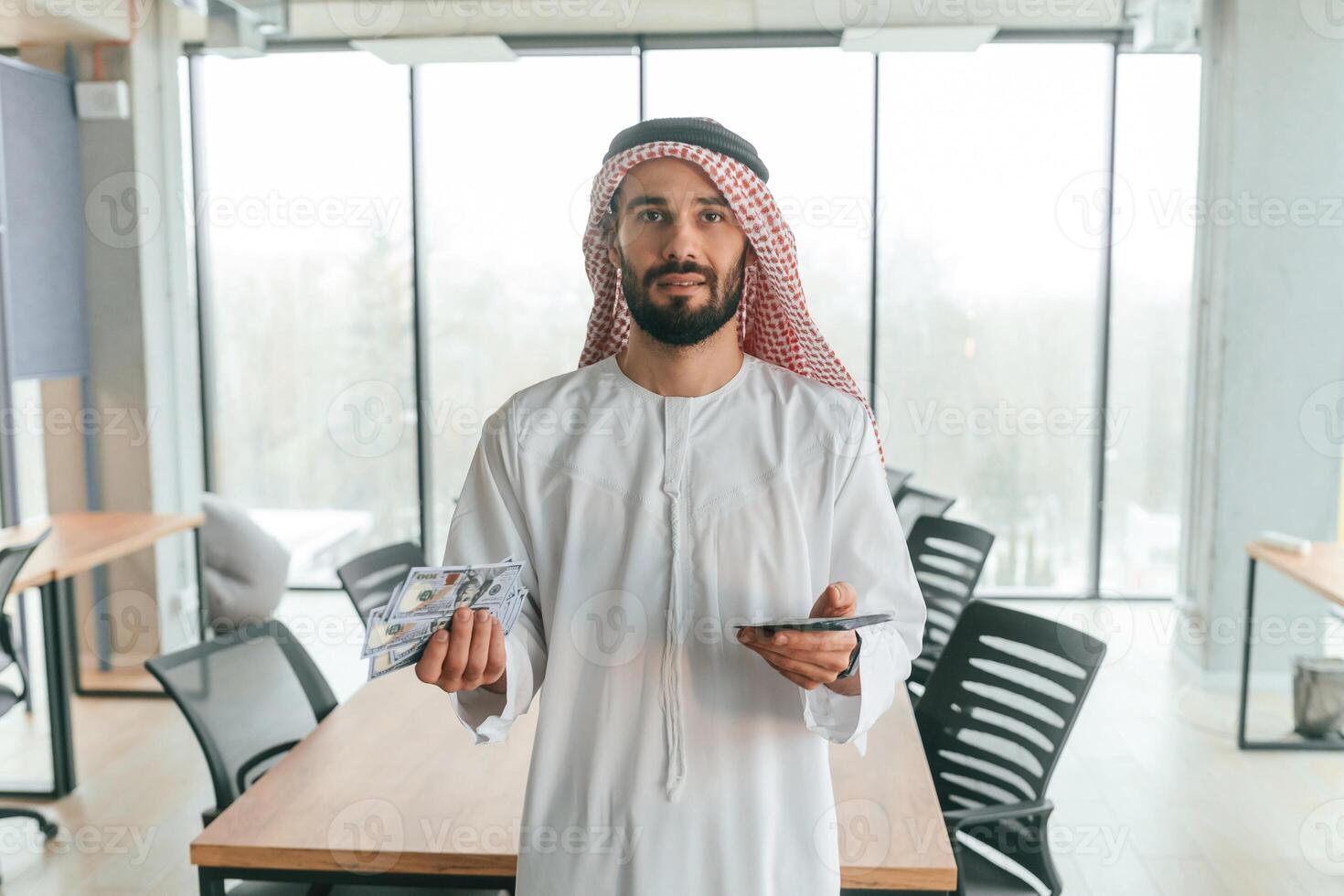 With smartphone in hand., Successful Muslim businessman in traditional outfit in his office photo