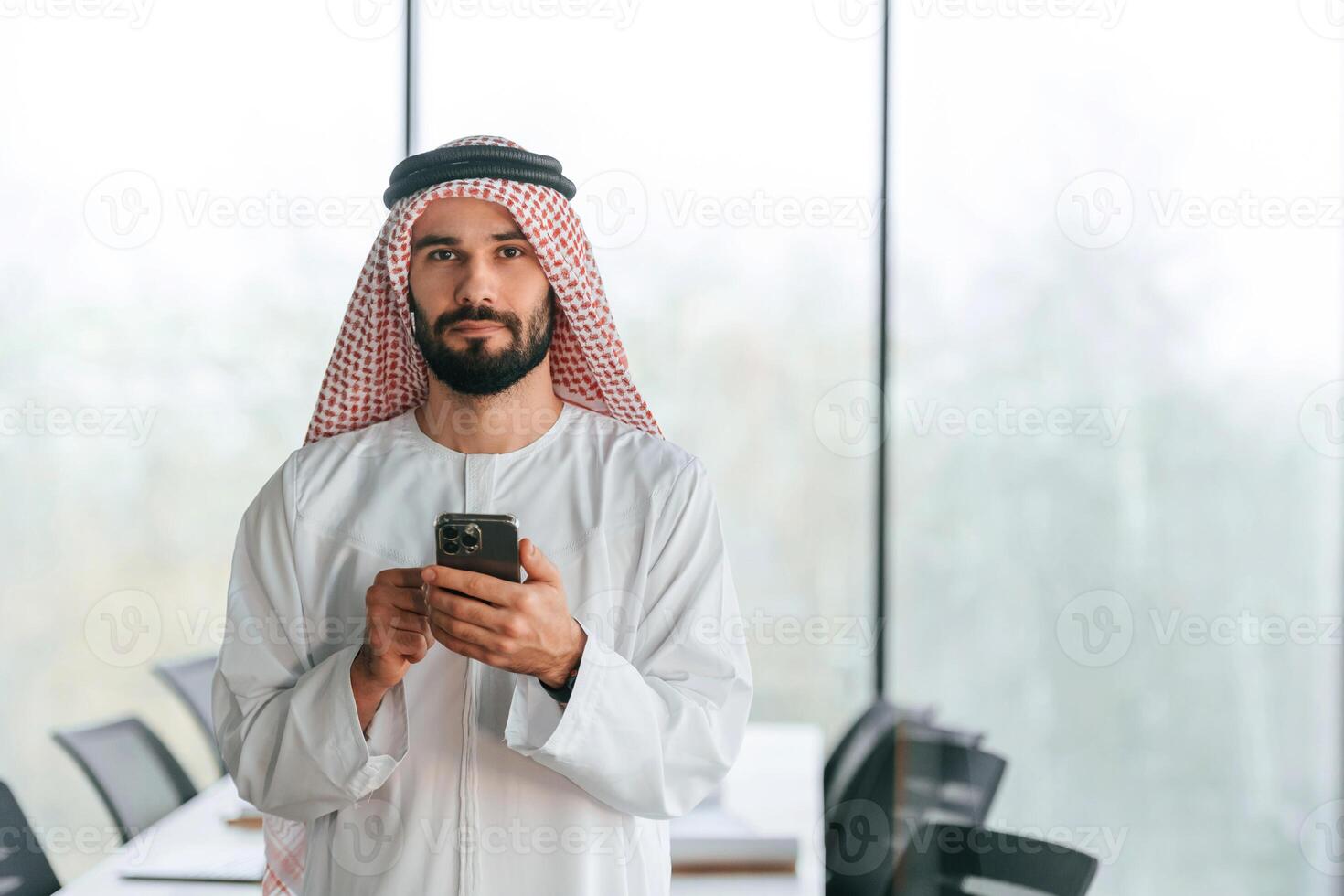 With, smartphone ,in ,hand. Successful Muslim businessman in traditional outfit in his office photo